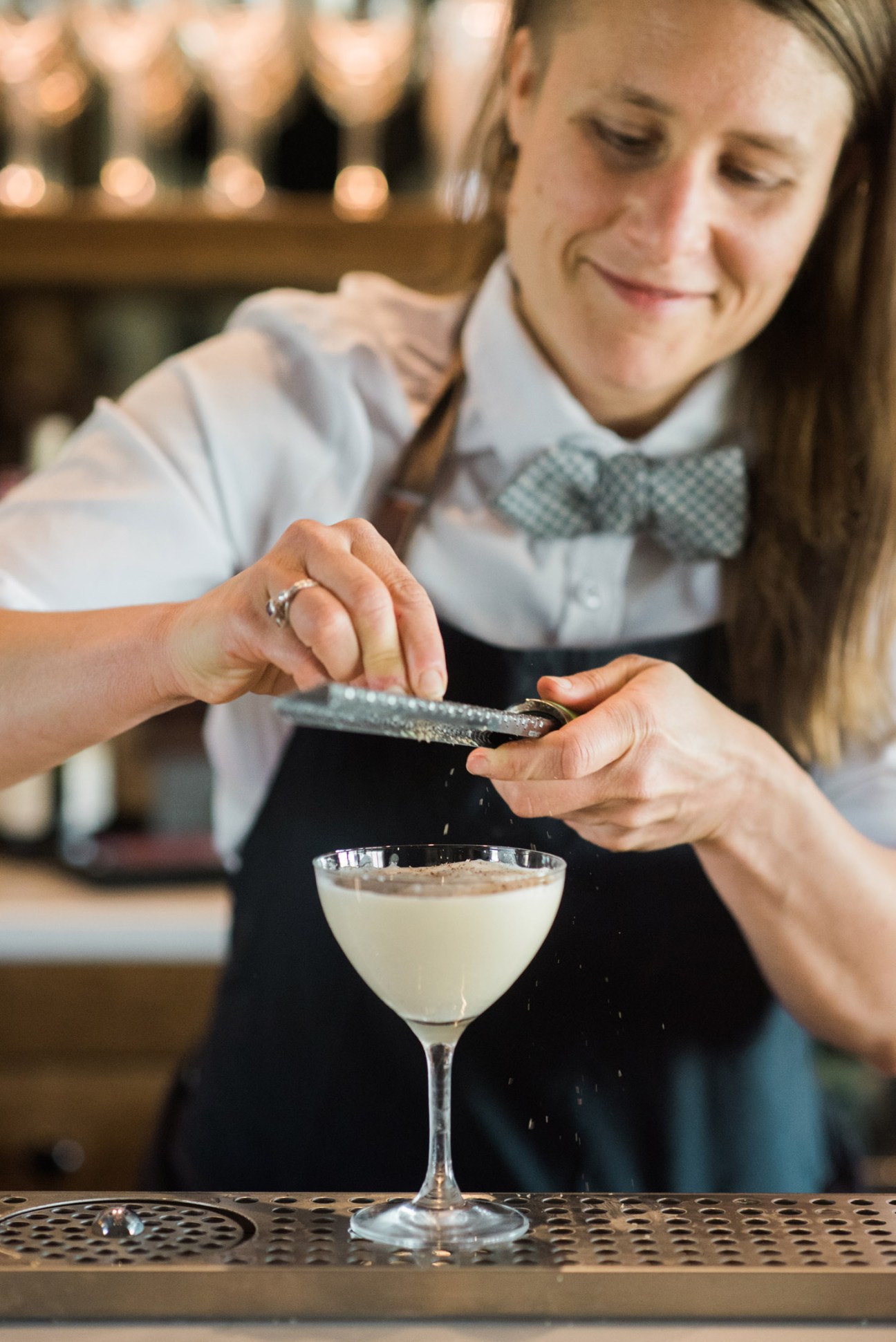 Bartender in white shirt and bow tie garnishes a pale cocktail with a citrus peel at The Clifton's Copper Bar.
