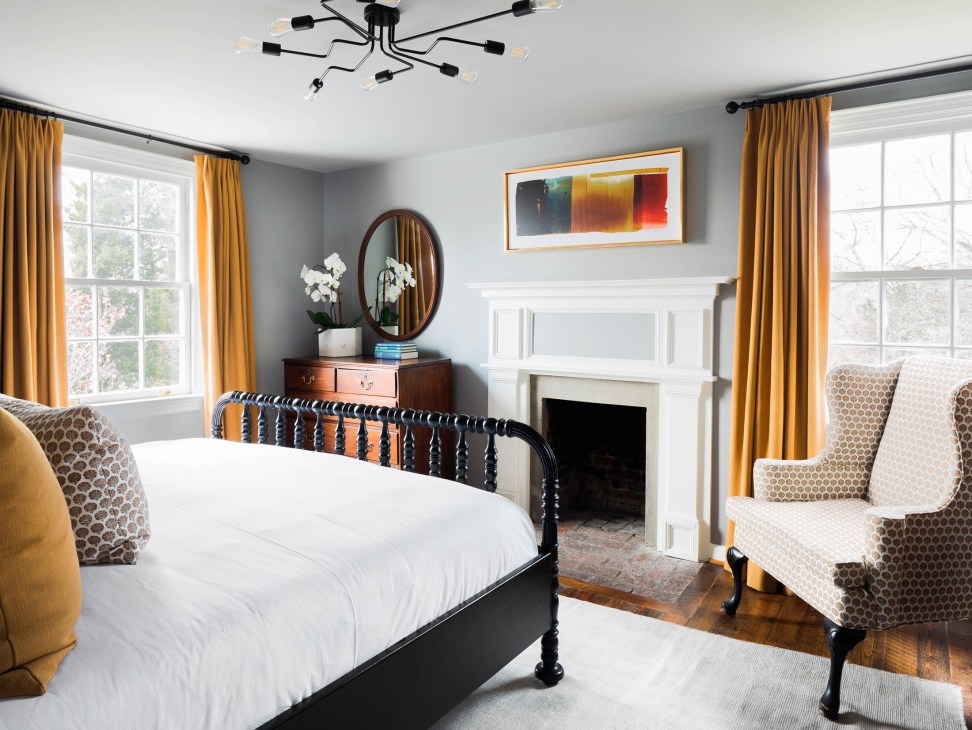 Elegant bedroom with black metal bed, white linens, gold curtains, and fireplace at The Clifton in Virginia.