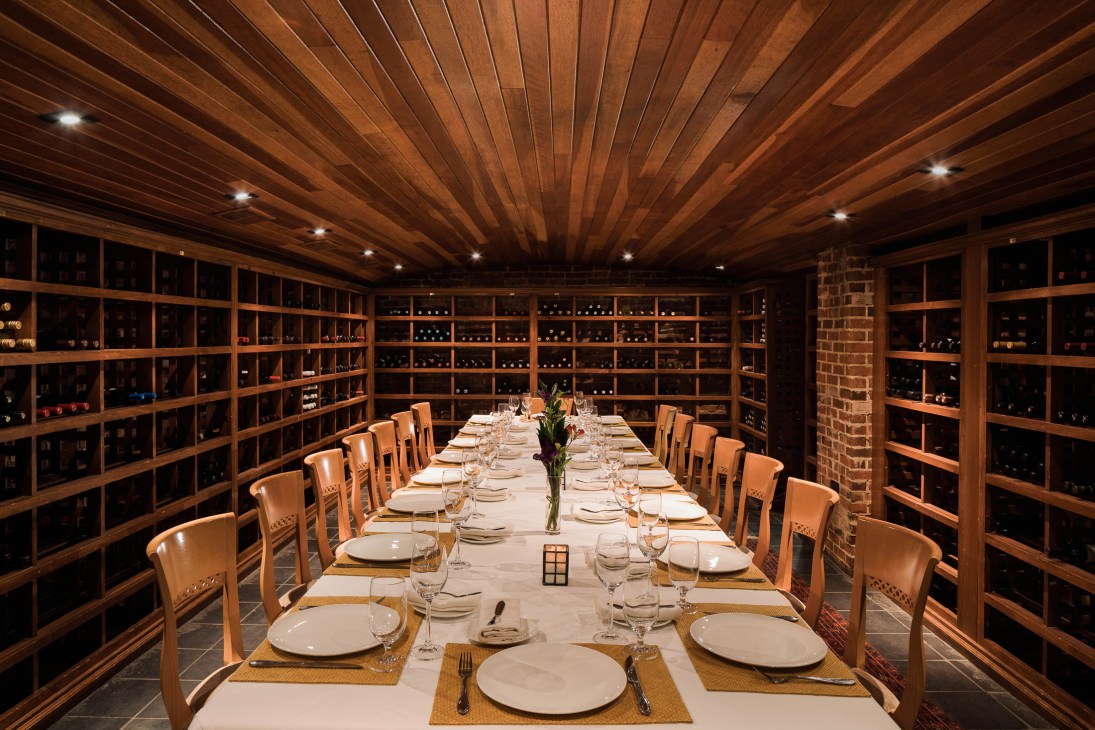 The Clifton's wine cellar with wooden shelving displaying bottles and a formally set dining table.