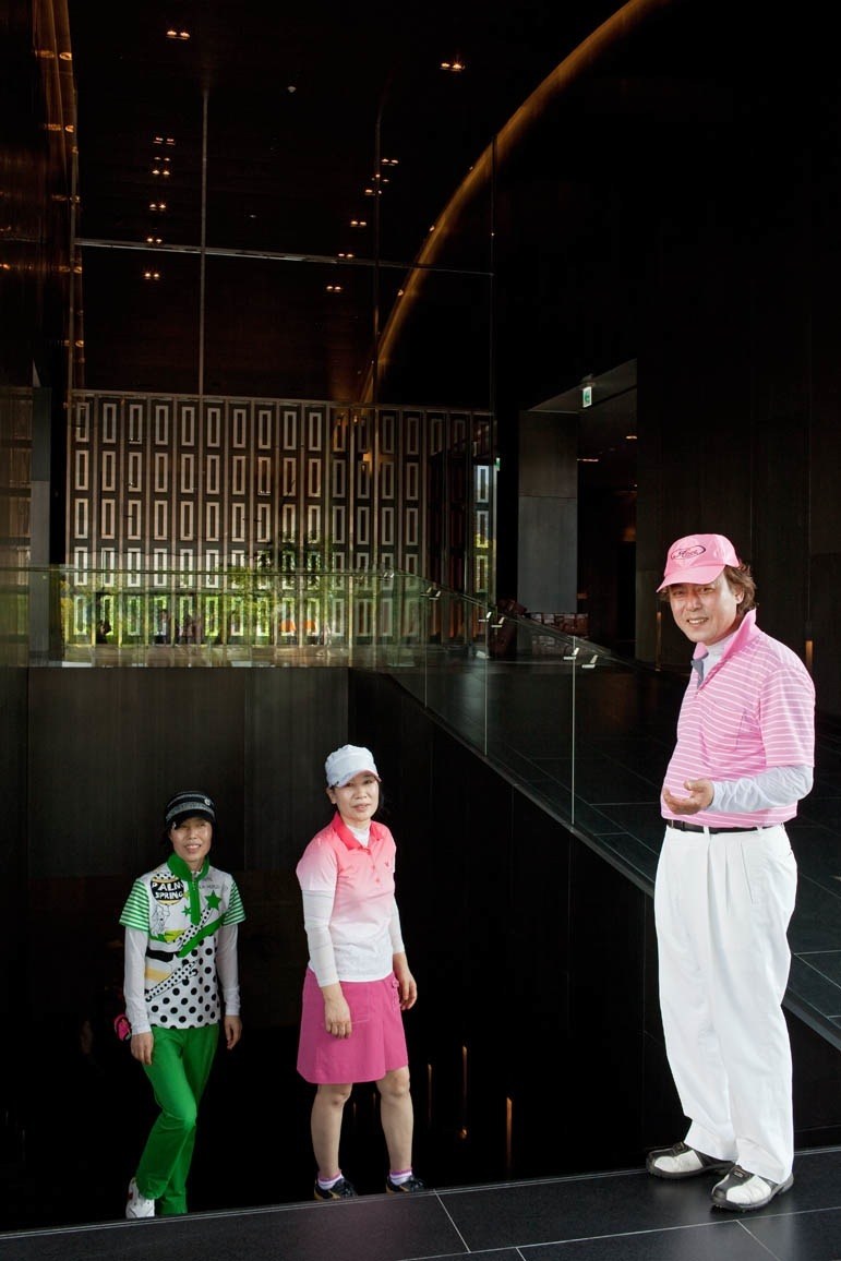 Three people in colorful golf attire standing in a modern dark interior space with illuminated signage.