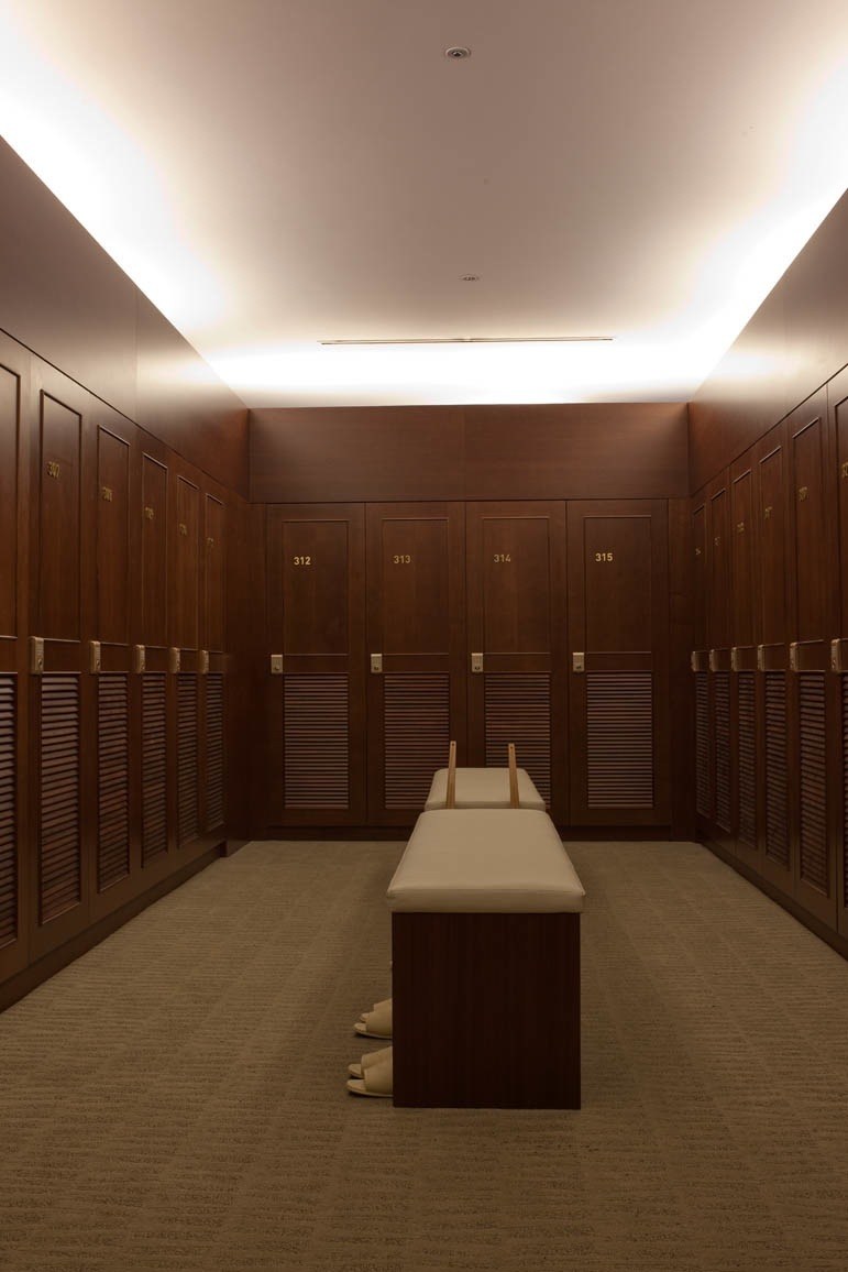 A luxurious changing room with dark wood lockers numbered 312-315 and cream-colored seating along a center bench.