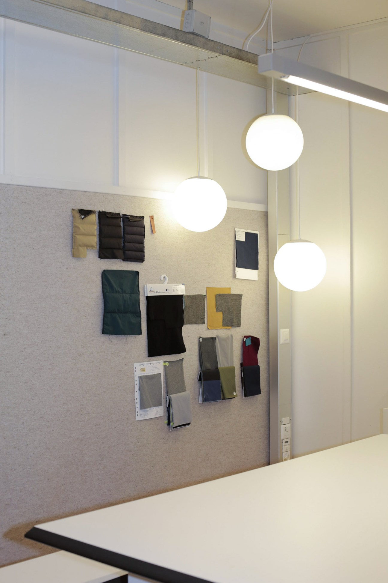 Wall display of fabric samples and material swatches under pendant lighting in DNS studio.