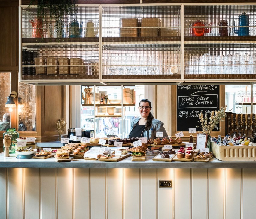 A barista stands behind the counter at Burr & Co coffee shop displaying fresh pastries and baked goods.