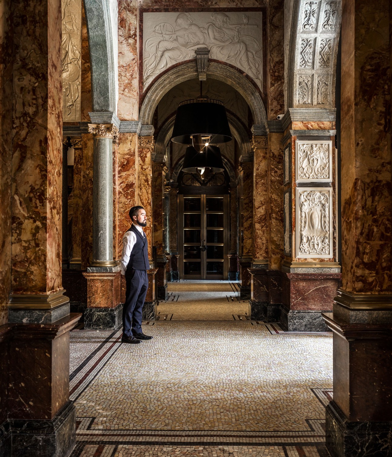 Man in suit standing in ornate marble hallway with columns, arches and decorative tilework at The Principal hotel