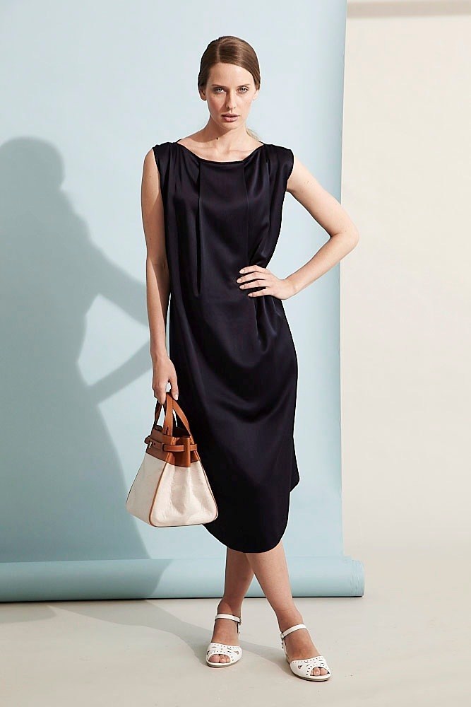 Woman wearing black sleeveless silk dress with brown and cream handbag and white sandals.
