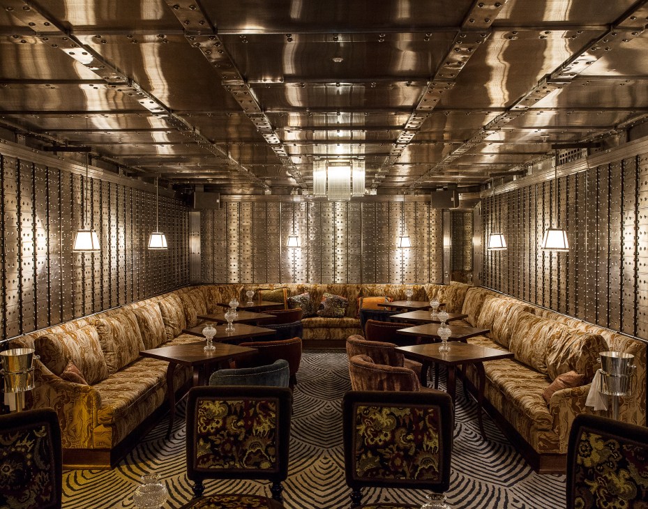 The Vault bar at The Ned with stainless-steel safety deposit boxes, upholstered seating, and a 20-tonne safe door.