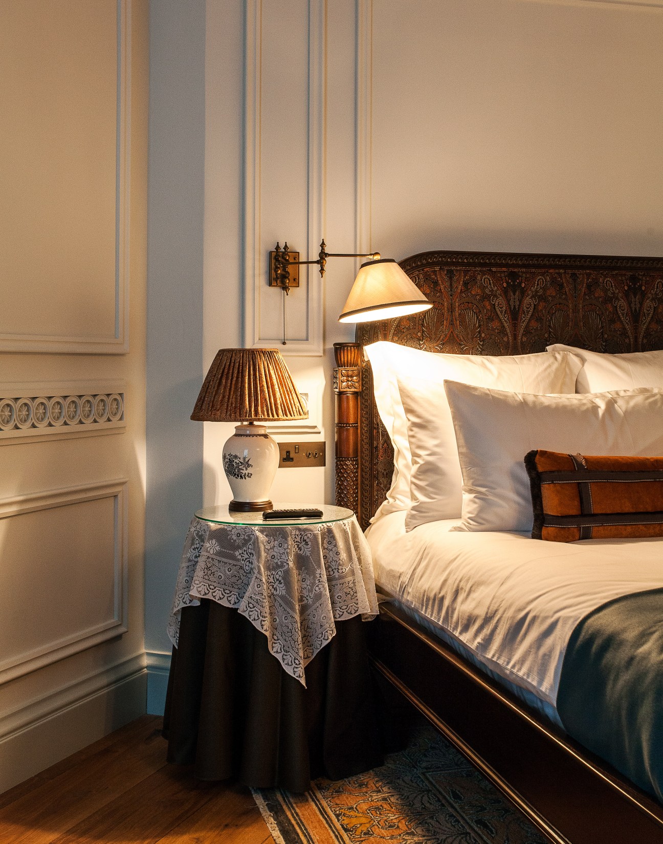A luxuriously appointed hotel bedroom at The Ned with ornate wooden headboard, period lighting, and cream bedding.