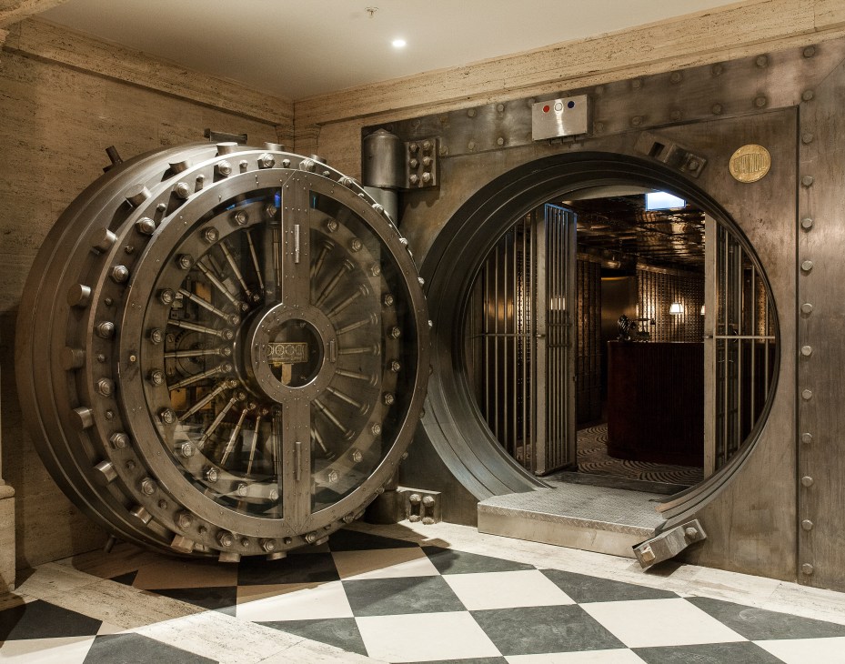 Entrance to The Ned's Vault bar featuring a large circular stainless-steel safe door and metal-studded walls.