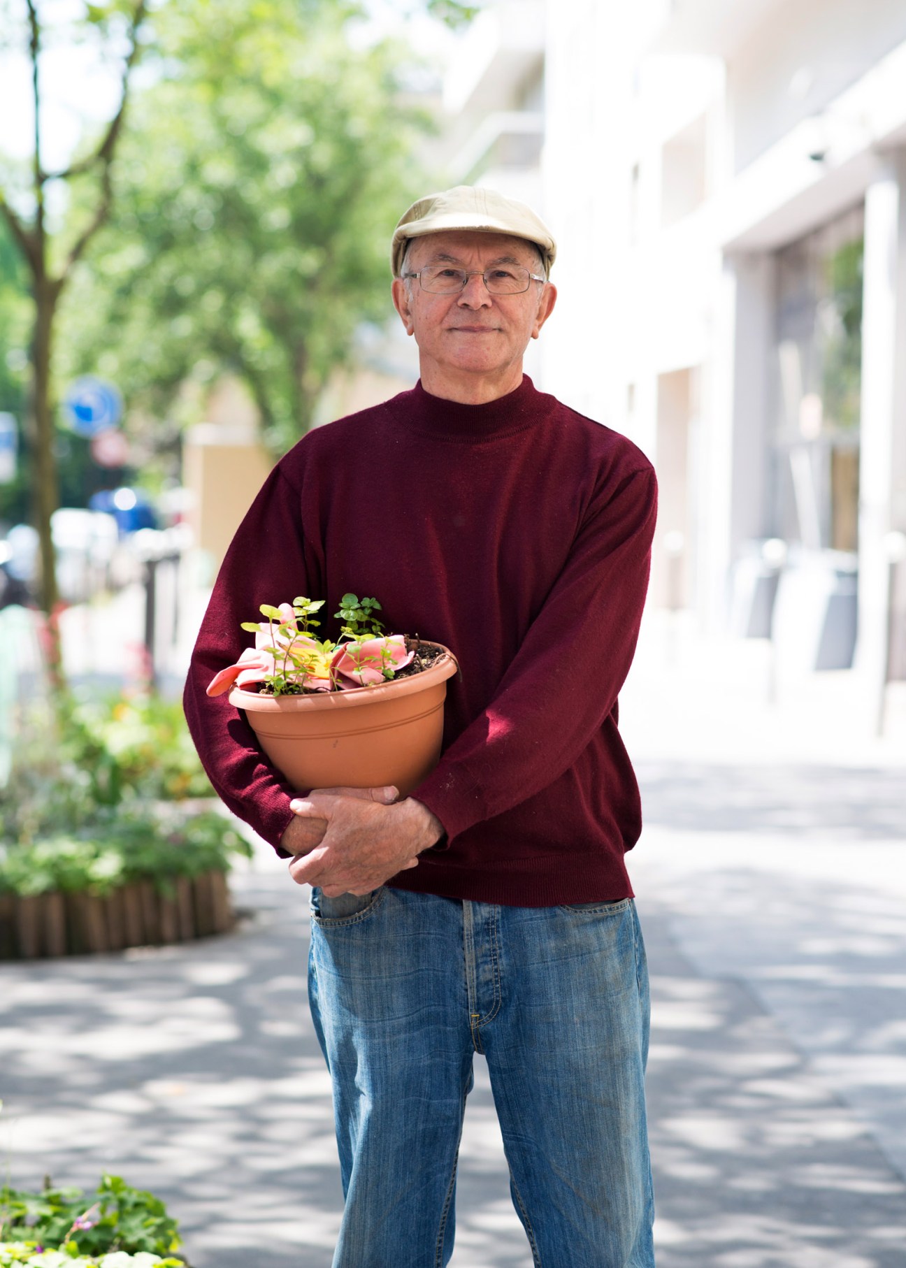Jean-Paul Potonet holds a potted flowering plant on a Paris street lined with trees.
