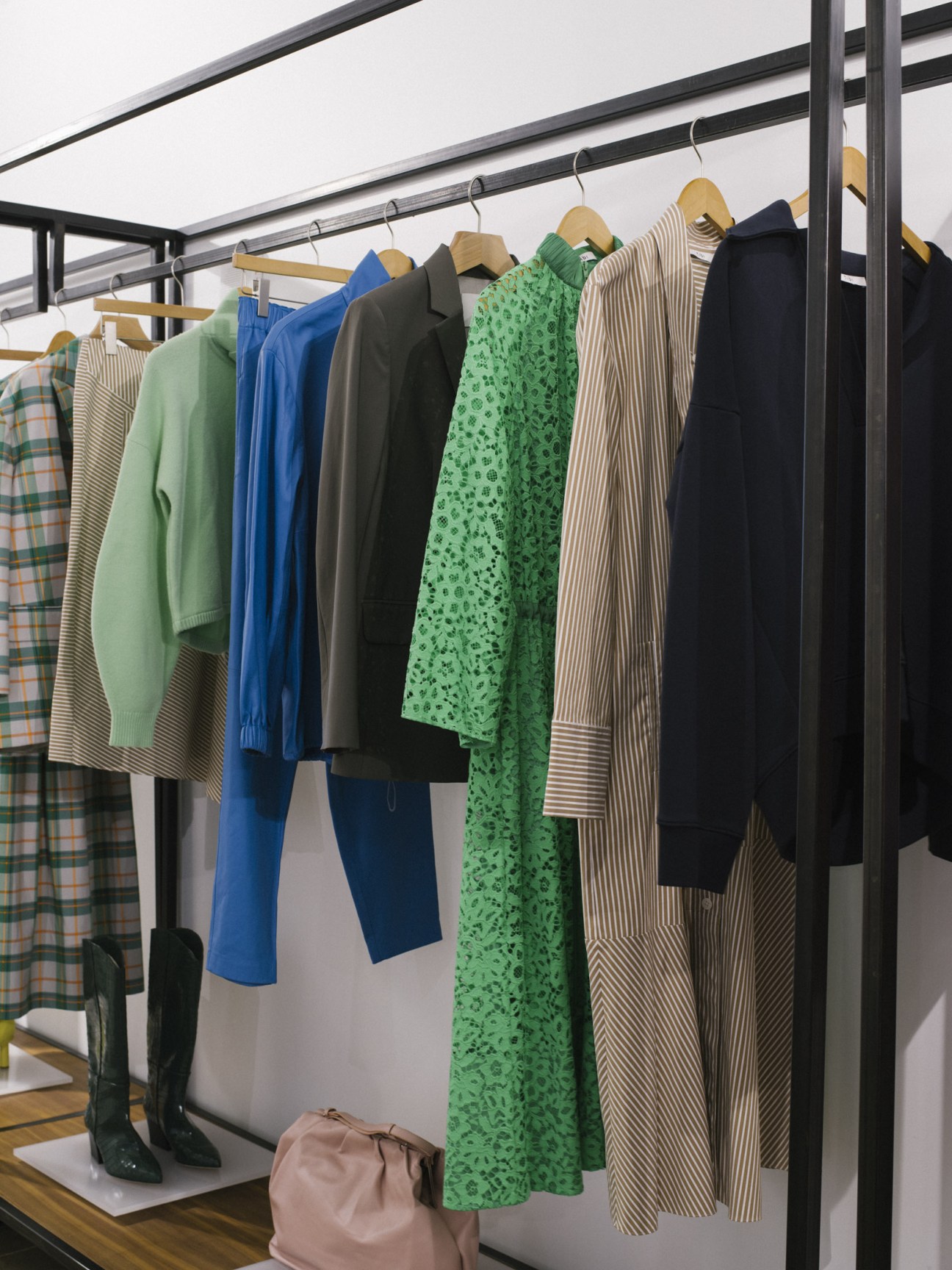 Tibi clothing collection displayed on wooden hangers including green knit, blue dress, olive blazer, green floral dress, and striped pieces.