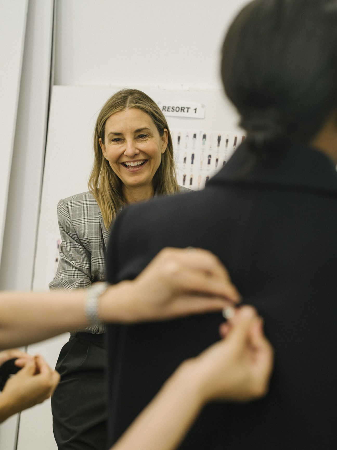 Amy Smilovic, founder and designer of Tibi, smiling in her Manhattan studio wearing a checked blazer.