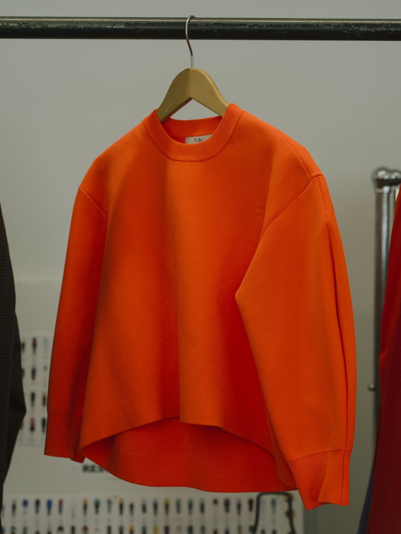 Tibi orange sweater hanging on wooden hanger in store display.