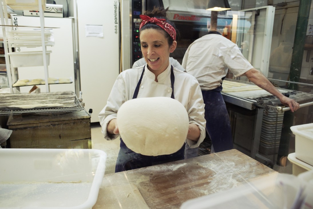 Baker holding a large round ball of dough in a professional bakery kitchen.