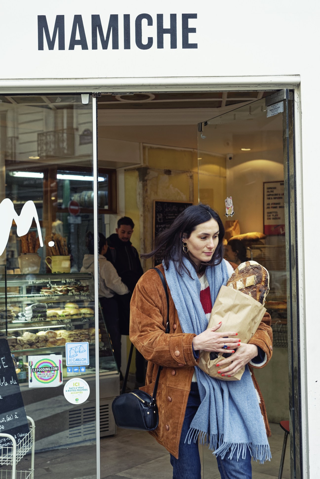 Customer leaving Mamiche bakery in Paris with bread in a paper bag