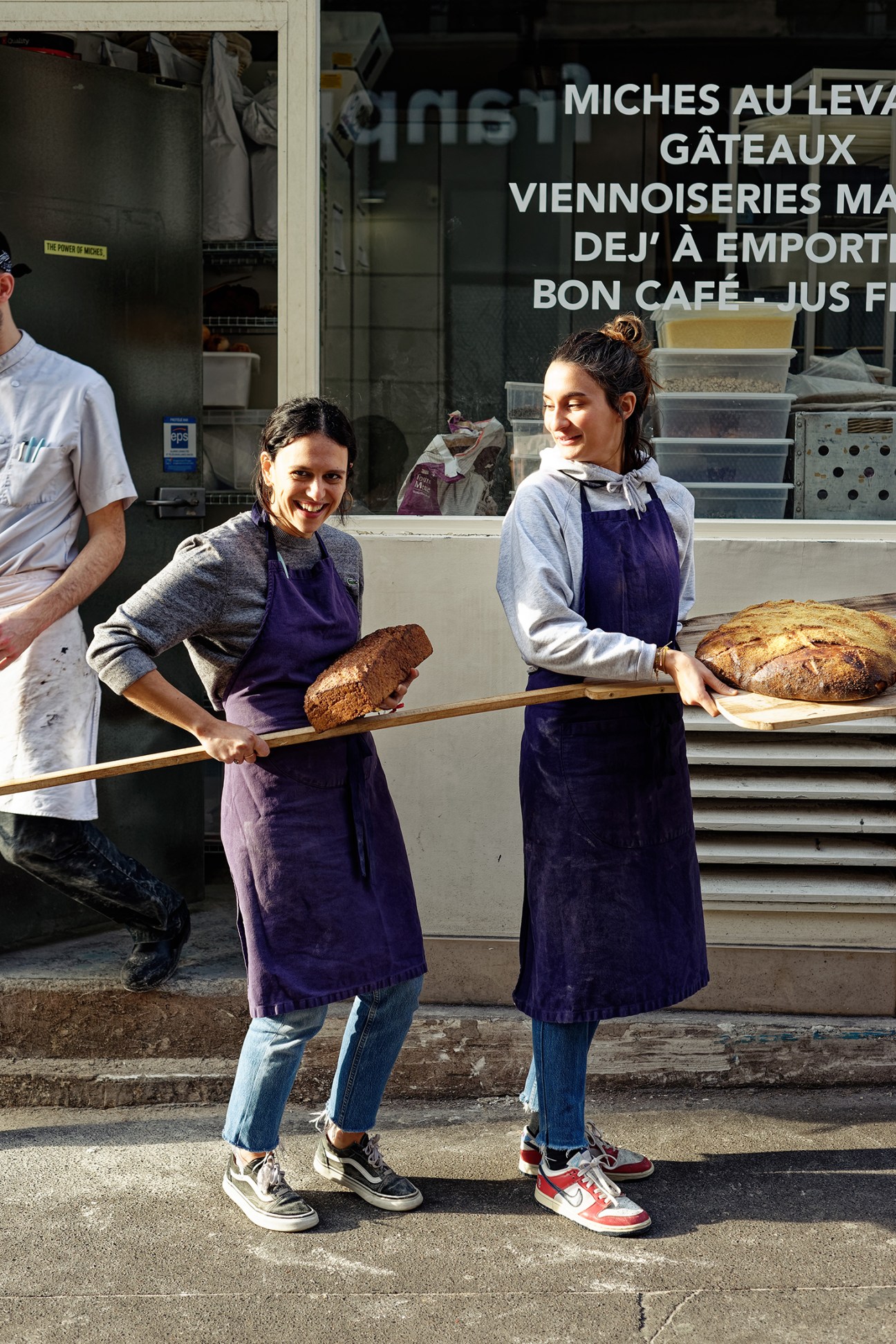 Victoria Effantin and Cécile Khayat, owners of Mamiche bakery, holding fresh bread on wooden peels outside their shop.