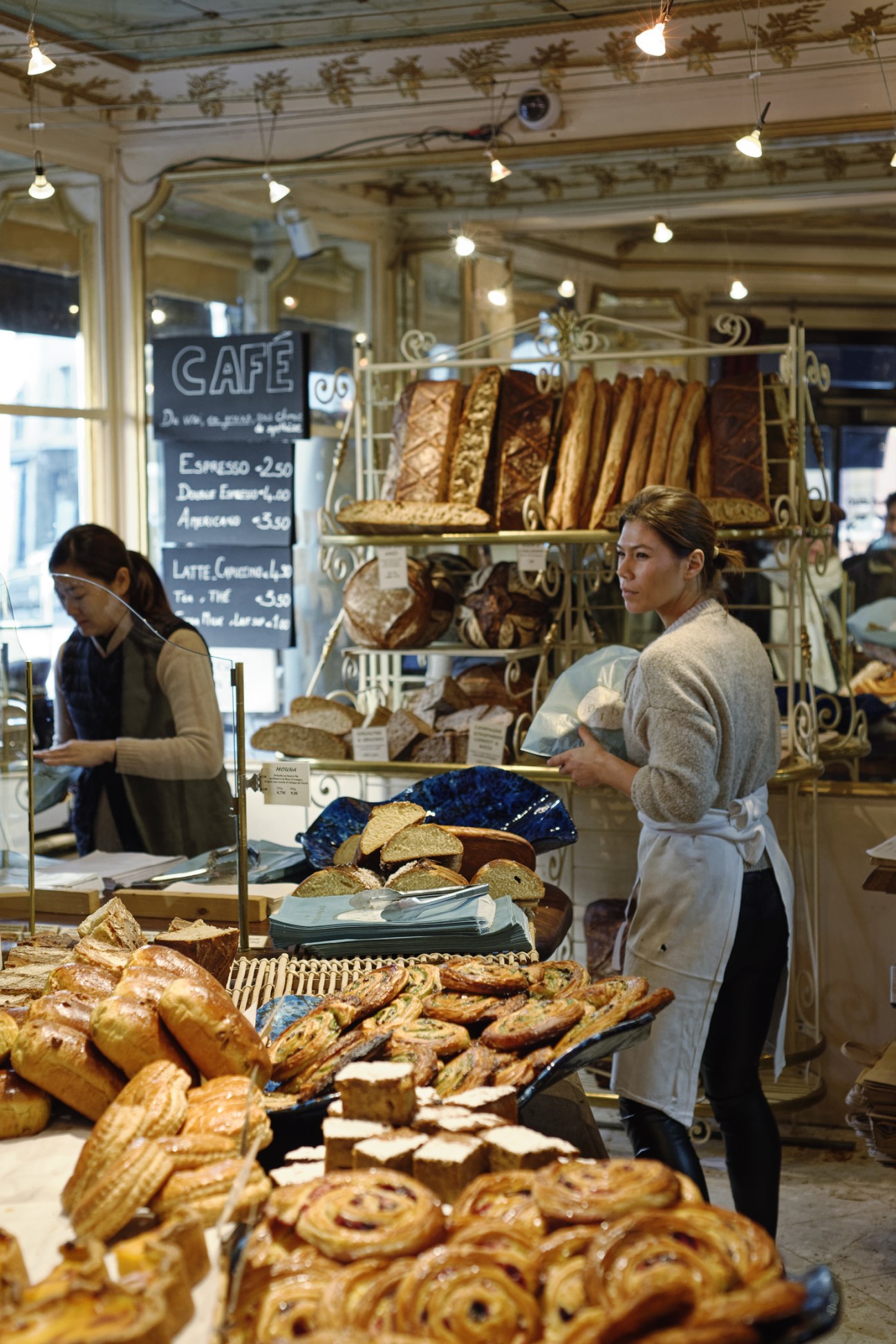 Woman shopping at Mamiche bakery counter with fresh bread and pastries on display.