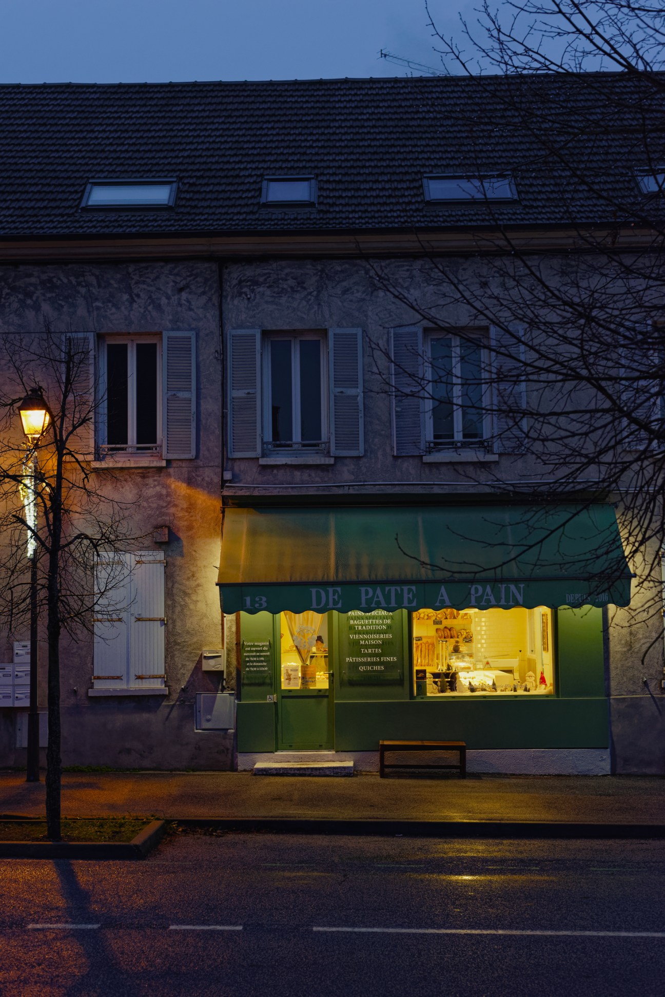 De Pâte à Pain bakery storefront in Pontchartrain with illuminated green awning at dusk.