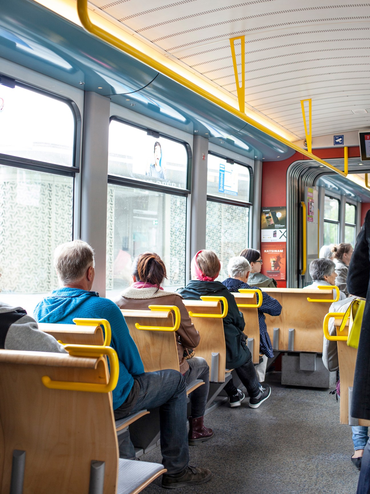 Passengers seated inside a tram with yellow handrails and grab poles looking out windows.