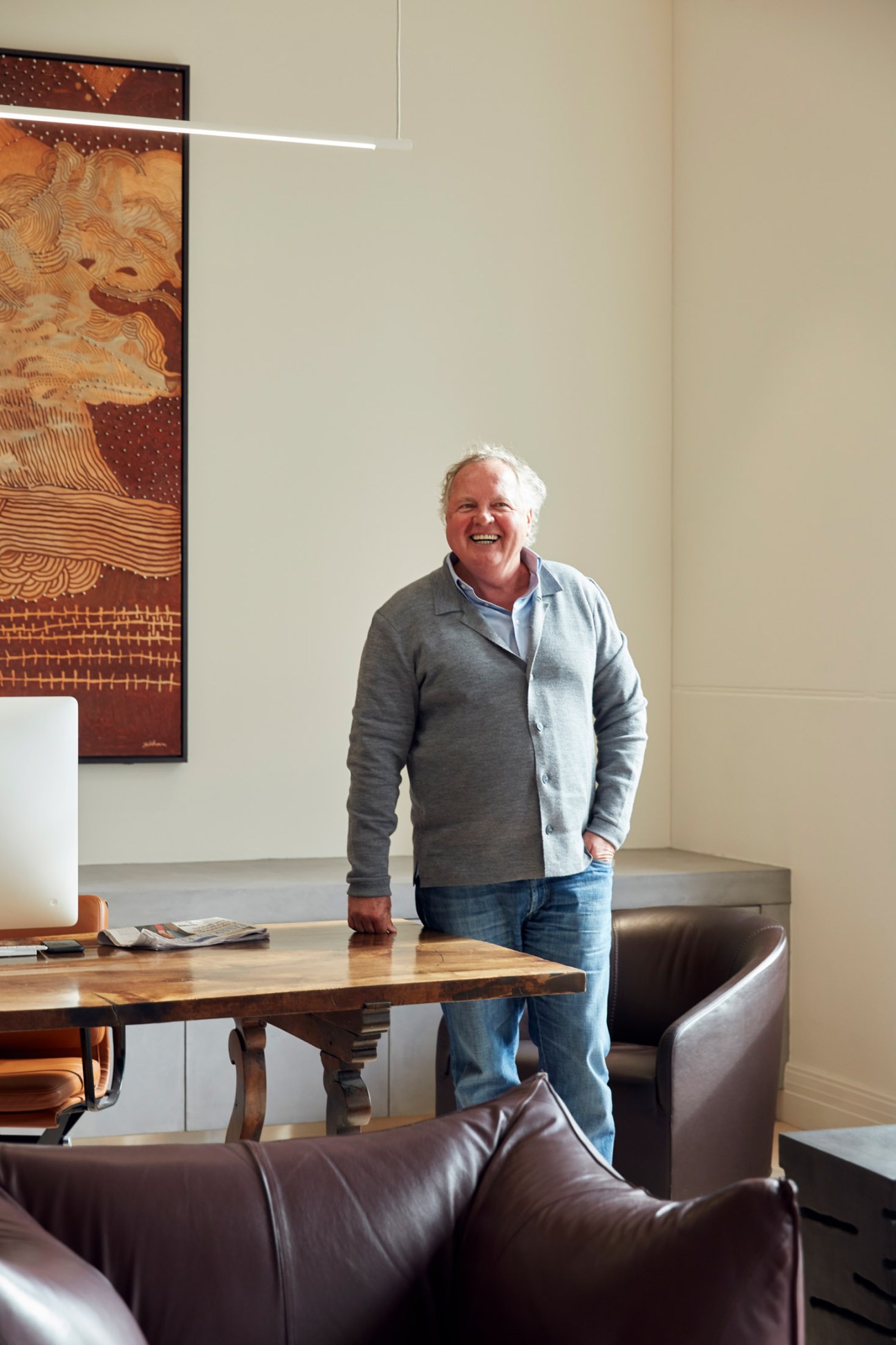 Pitzy Folk standing beside a wooden table in his office with leather chairs and artwork on the wall
