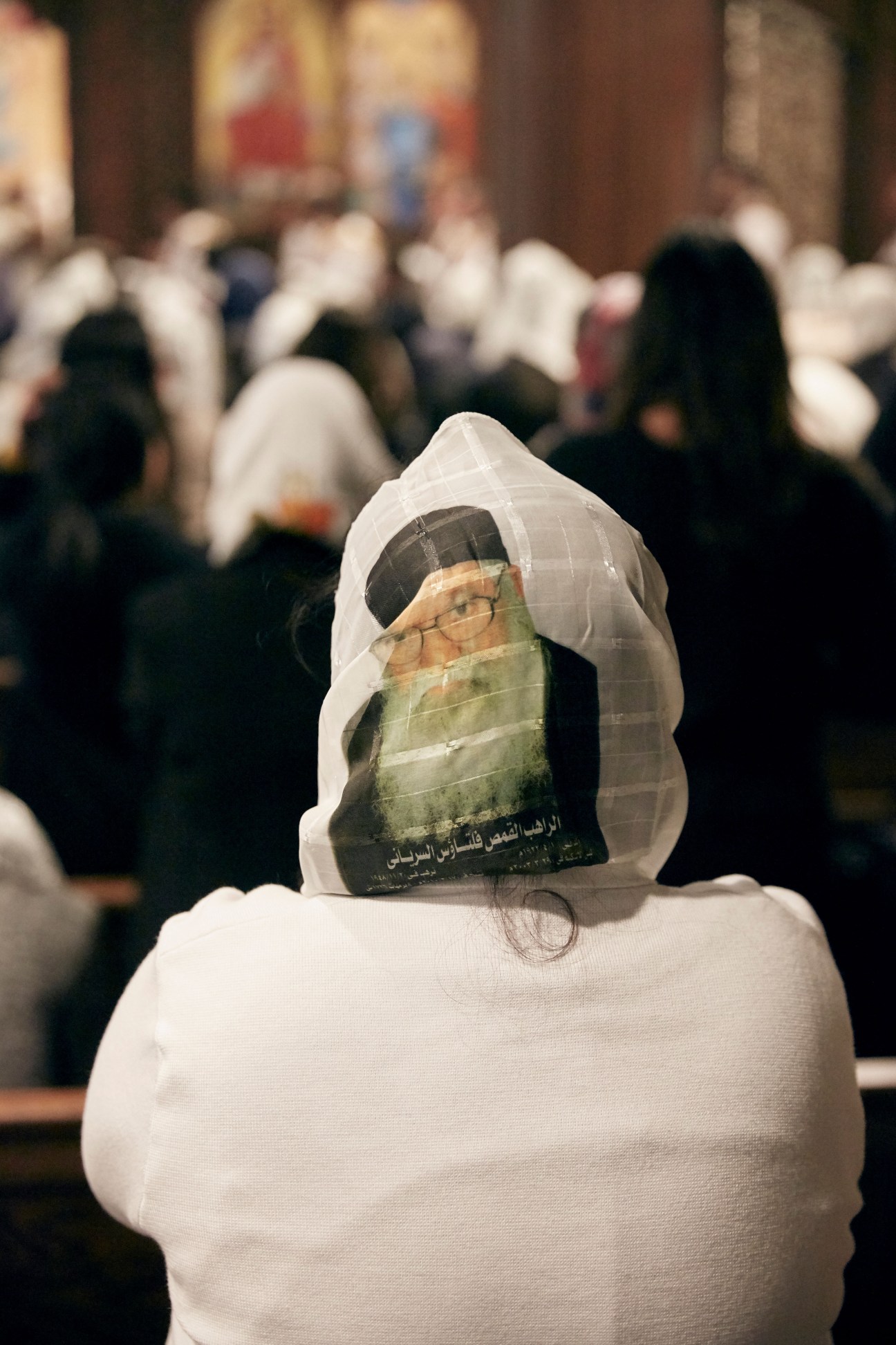 A Coptic worshipper wearing white clothing holds an image of a religious figure during a church service.