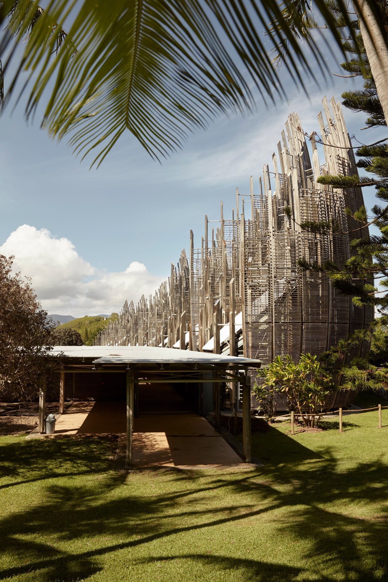 Tjibaou Cultural Centre's distinctive shell-shaped structures designed by Renzo Piano, with palm fronds overhead and manicured grounds.