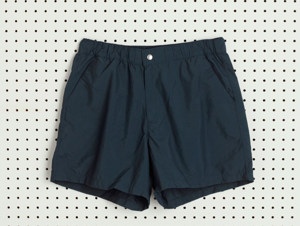 Navy blue swim trunks with elastic waistband displayed on a polka dot background.
