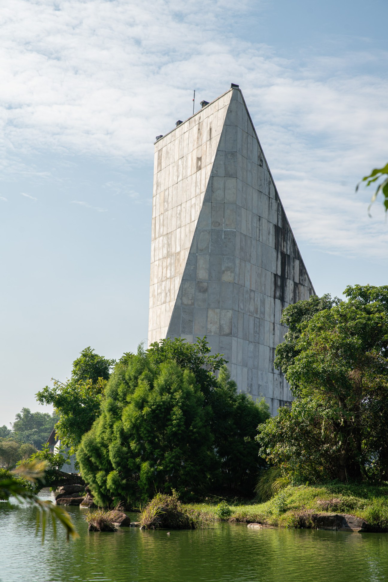 Polyhedral concrete tower of As-Sobur Mosque rising above jungle vegetation and water in Indonesia.