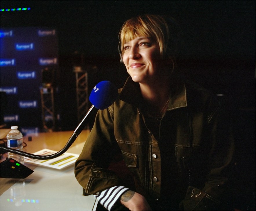 Europe 1 presenter Daphné Bürki at a radio studio microphone wearing a brown jacket.