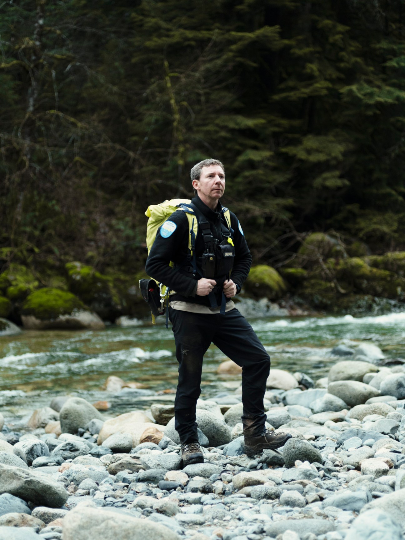 Park ranger Rich Wheater hiking on rocky terrain beside a flowing creek in Vancouver wilderness