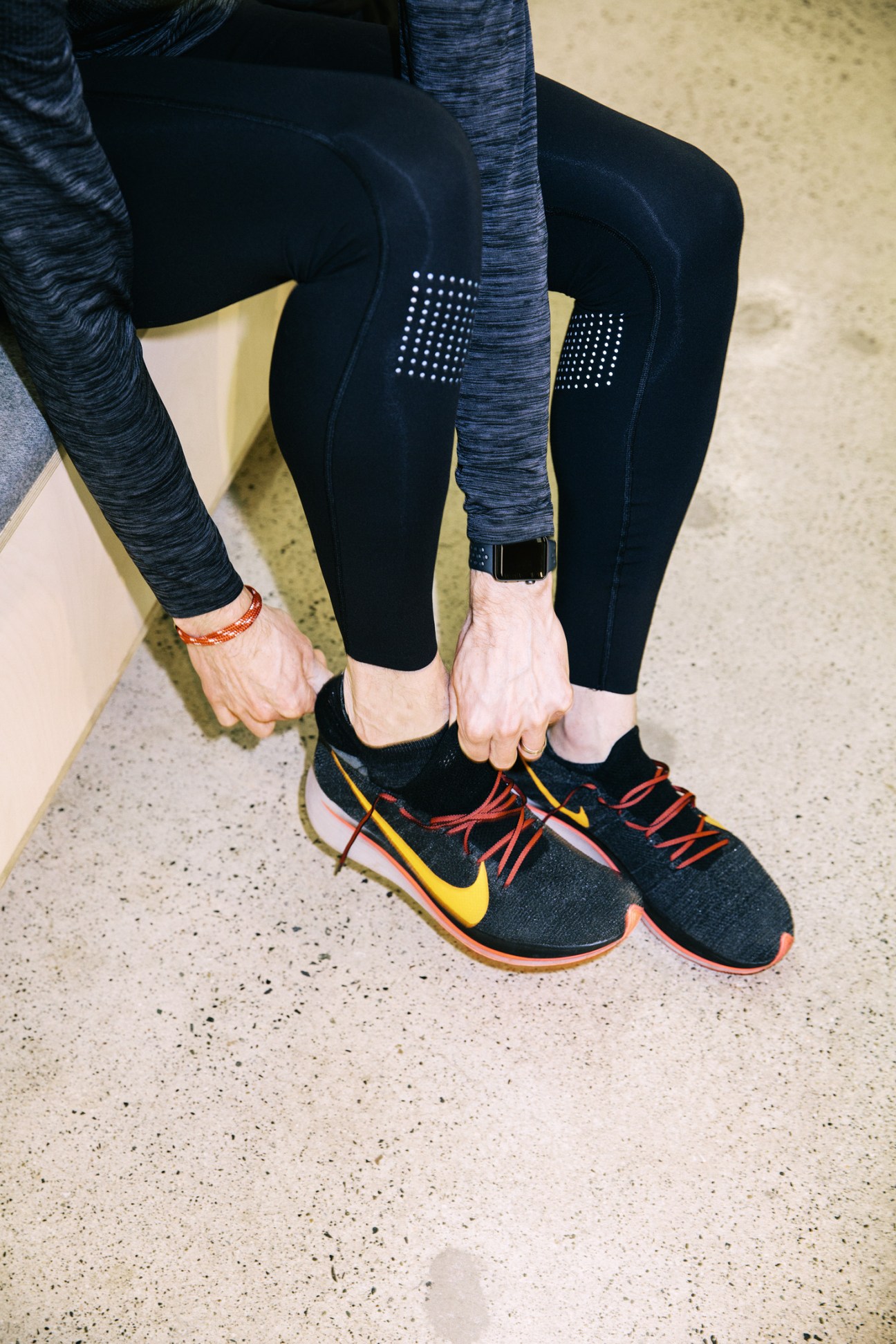 Runner wearing Nike Zoom Flyknit shoes with black leggings and blue top, touching laces before run.