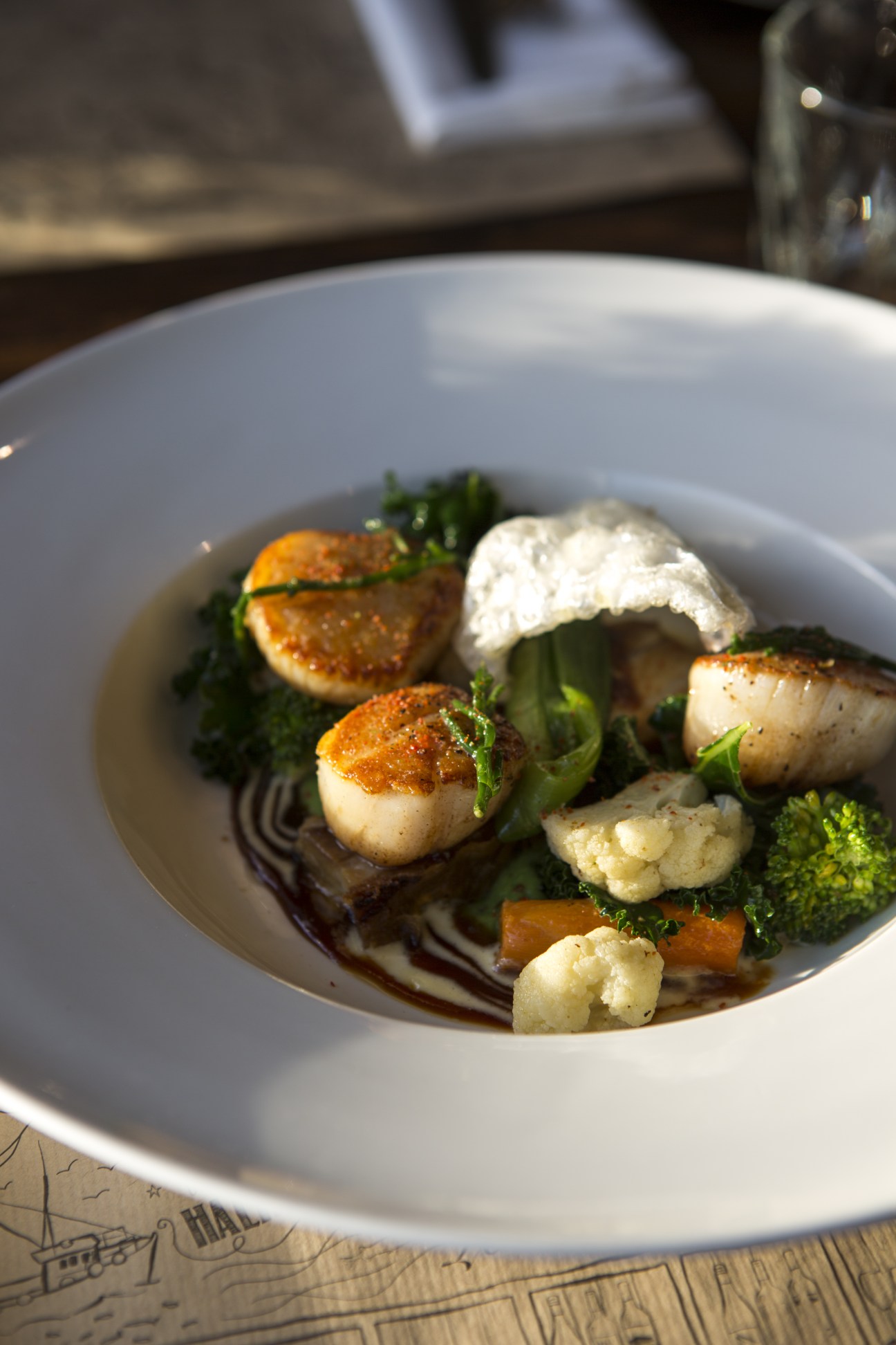 Seared scallops with broccoli, cauliflower and pork on a white plate at Dulse & Brose restaurant.