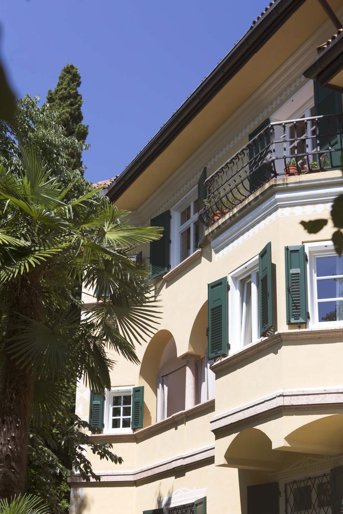 Exterior of Villa Arnica showing the mustard yellow facade with green shutters and ornate balconies.