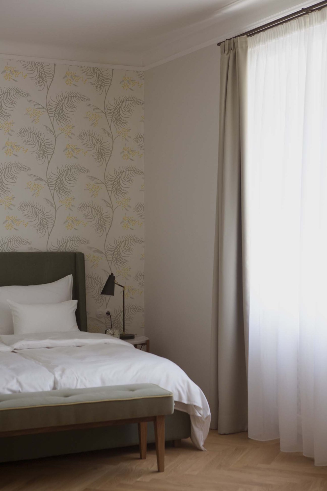 A minimal guest bedroom at Villa Arnica with a bed, botanical wallpaper, and large window with sheer curtains.