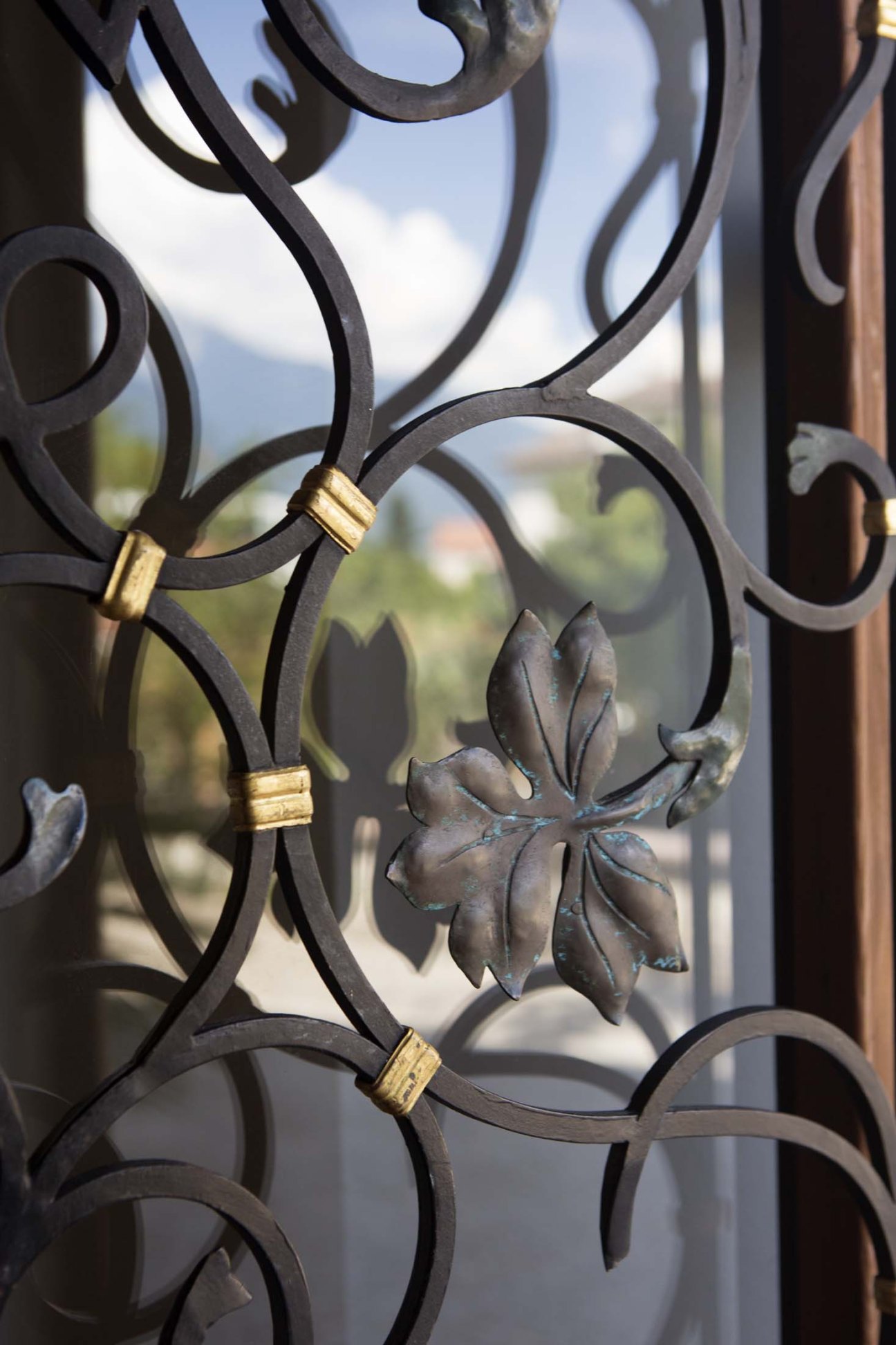 Close-up of ornamental wrought-iron grille with gold-plated accents and mountain views beyond.