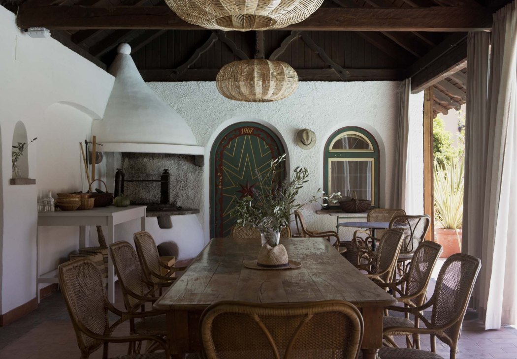 Communal dining area at Villa Arnica with original terrazzo flooring, woven pendant lights, and rattan chairs around a wooden table.
