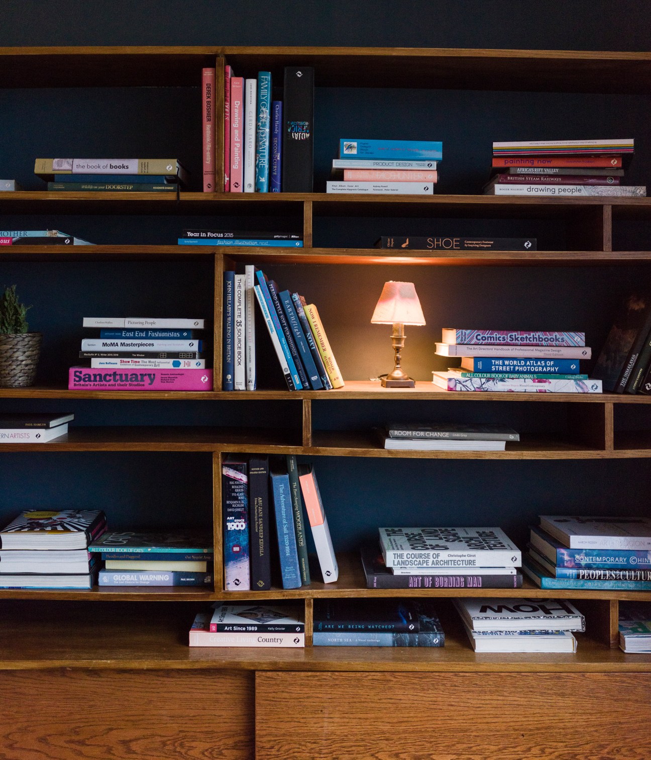Wooden bookshelf with books organized by color and subject, featuring a small brass lamp in the center