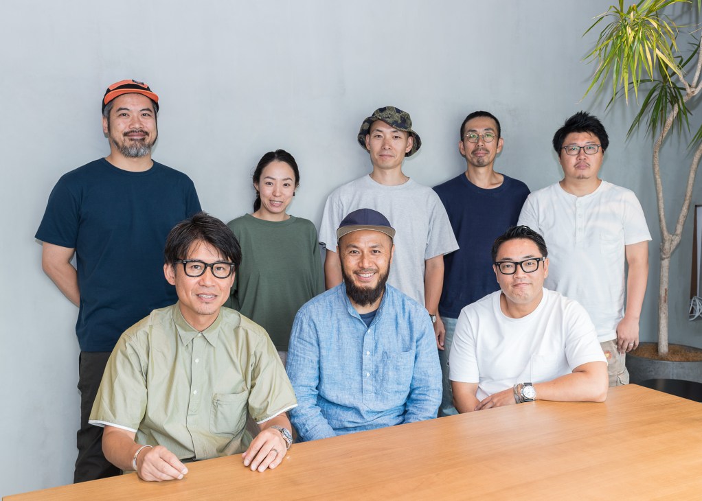 Eight members of the Woolrich Outdoor design team pose together in a studio with a potted plant.