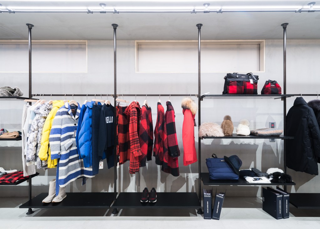 Woolrich Outdoor collection displayed on black metal shelving with jackets, coats and accessories in red, blue, yellow and neutral tones.