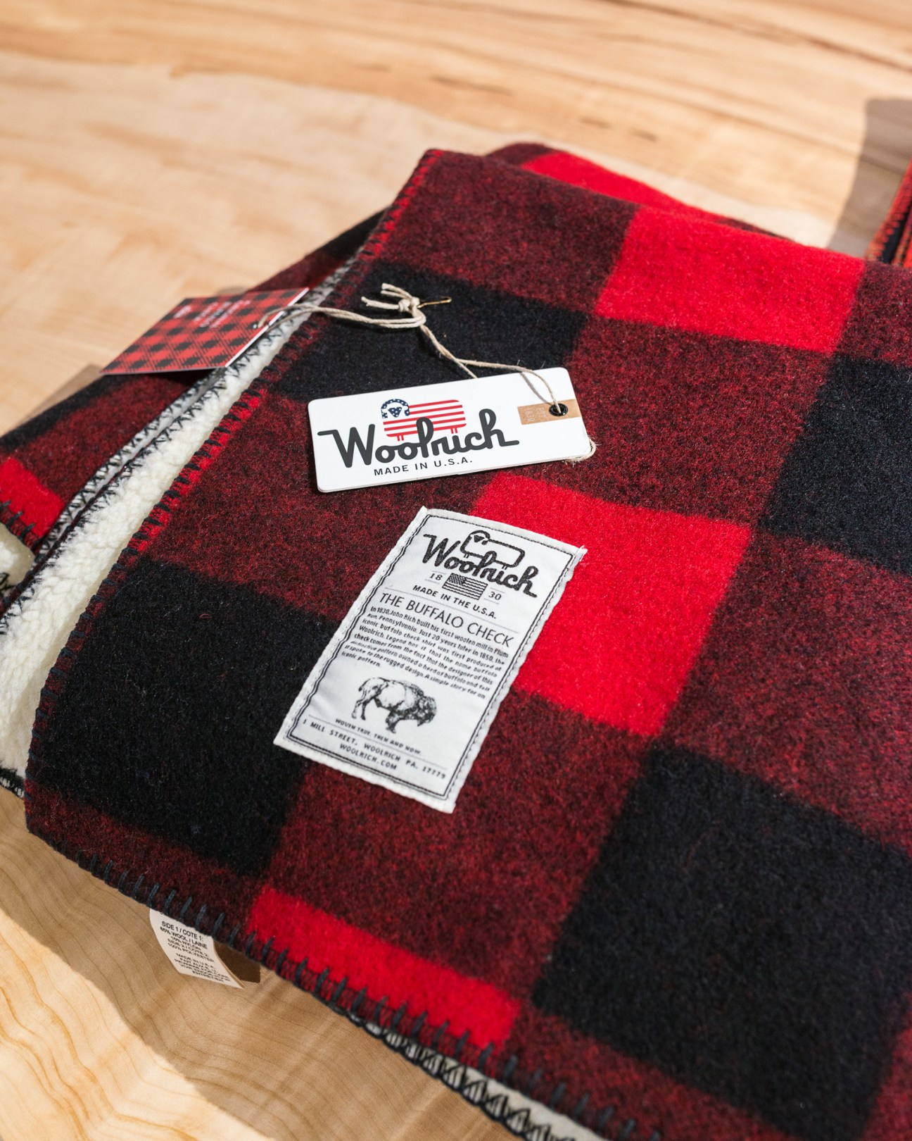 Red and black buffalo check Woolrich blanket with brand labels displayed on wooden floor.
