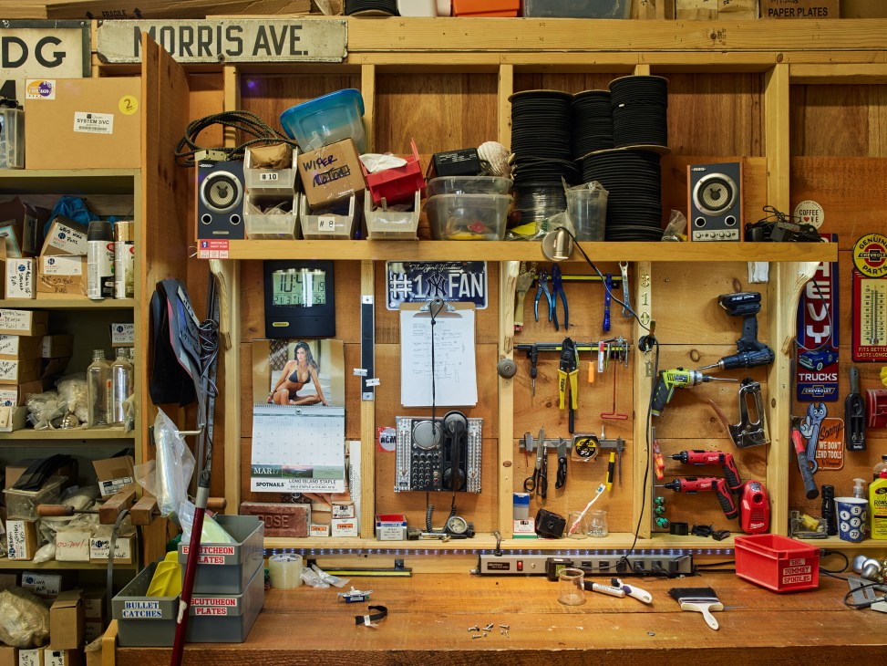 A cluttered workbench with tools, speakers, cables, and miscellaneous items organized on pegboard and shelves.