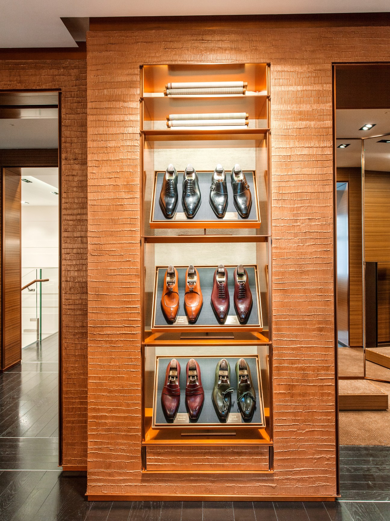 Illuminated display of polished dress shoes in various colors arranged on shelves within a honeyed rosewood cabinet at Zegna's London flagship store.