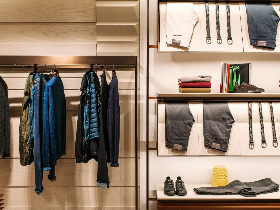 Interior of Zegna London flagship store displaying jackets on hangers and folded clothing and accessories on shelves.