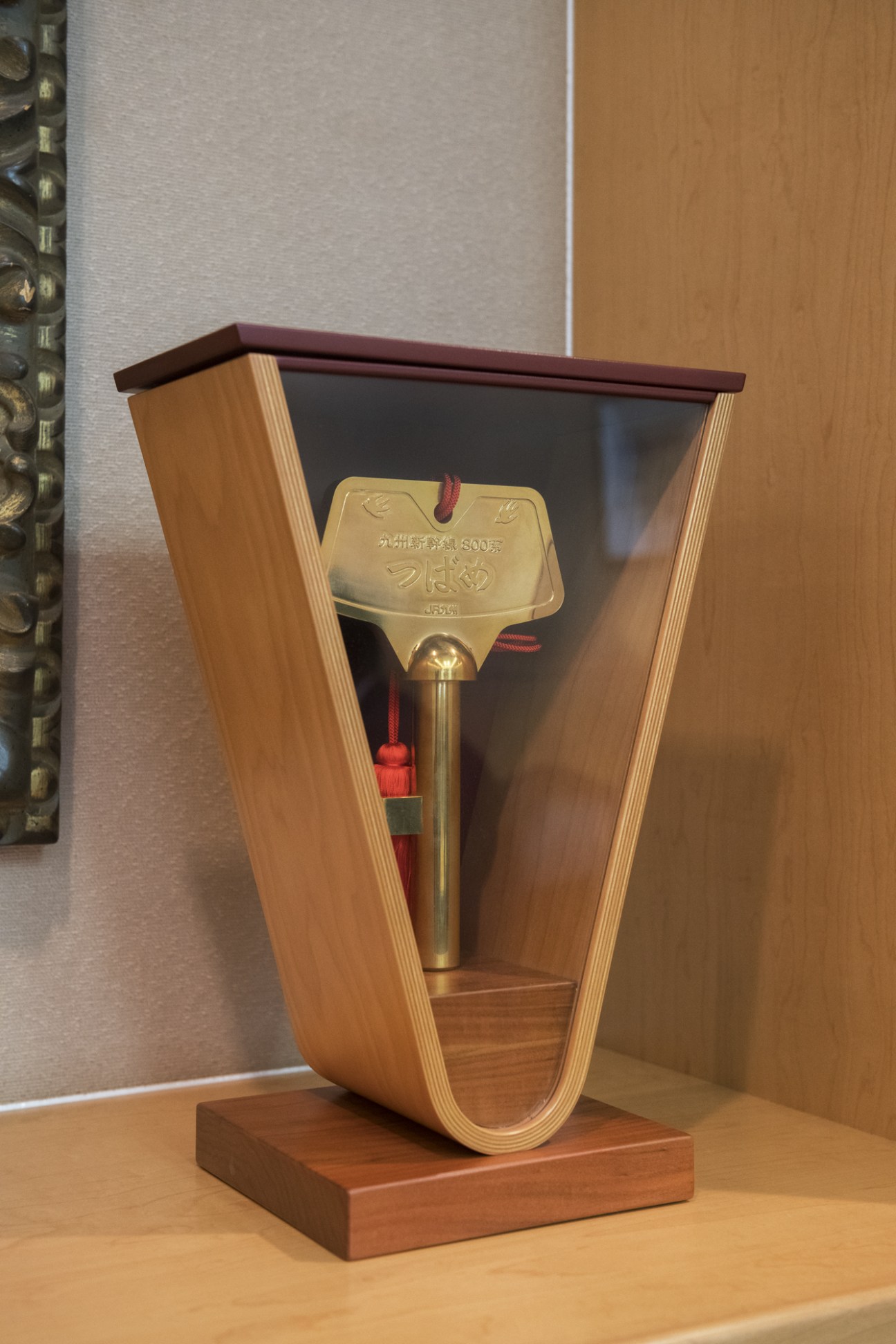 Gold ceremonial key displayed in wooden case with dark burgundy top and red cord.