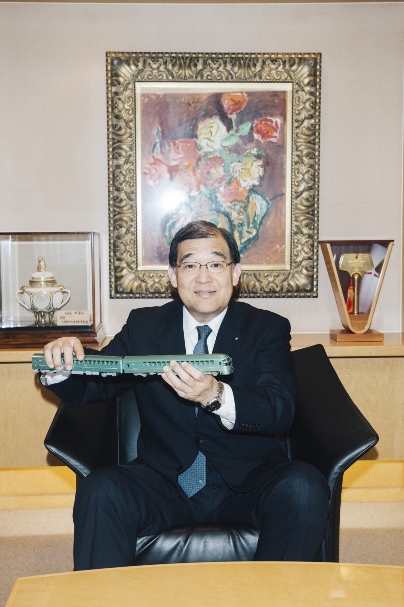 Koji Karaike, chairman of JR Kyushu, holds a model train car while seated in his office.