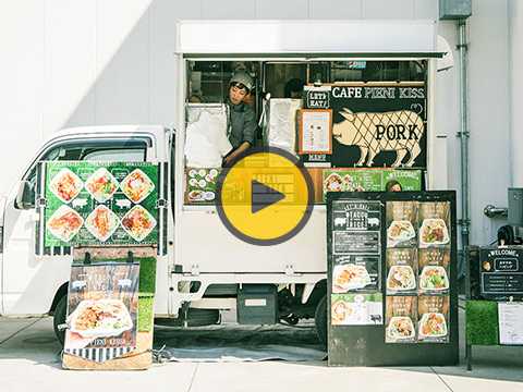 White food truck with green accents displaying colorful packaged meals and signage.