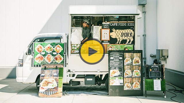 A food truck with green and white exterior displaying menu items and signage for pork dishes.