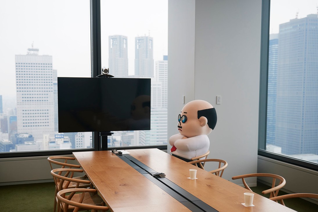 Line character Boss, a bald figure with glasses, sits at a conference table overlooking Tokyo's skyline.