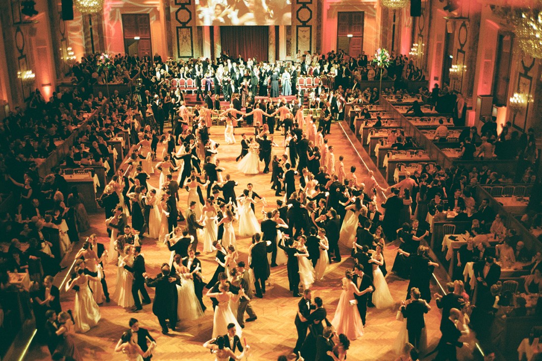 Aerial view of formal ballroom with hundreds of couples in evening wear waltzing on ornate dance floor