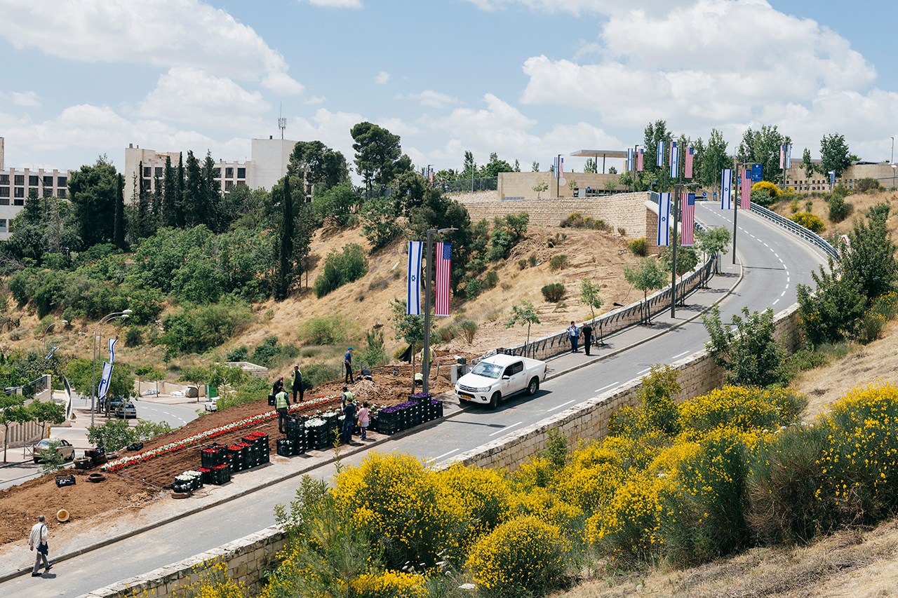 The US embassy in Jerusalem with Israeli and American flags displayed on poles along a curved road.