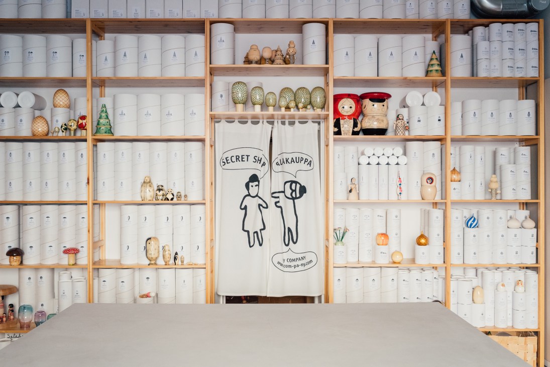 Wooden shelving unit displaying white containers, ceramics, wooden toys and decorative items at Salakauppa shop in Helsinki.